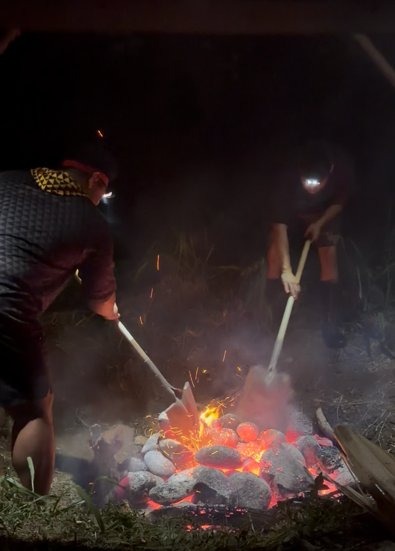 Imu (traditional Hawaiian underground oven) being prepared at the Hālau Kaʻeaikahelelani farm in Keauhou — glowing lava rocks and fire at night