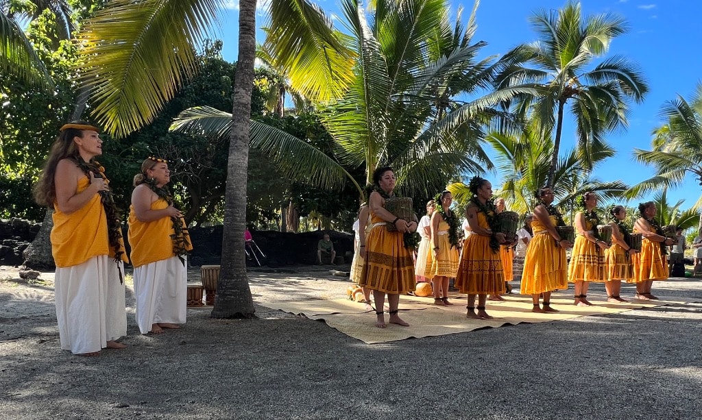 Hālau Kaʻeaikahelelani performing at Puʻuhonua o Hōnaunau, Kona — dancers in yellow dresses beneath palm trees